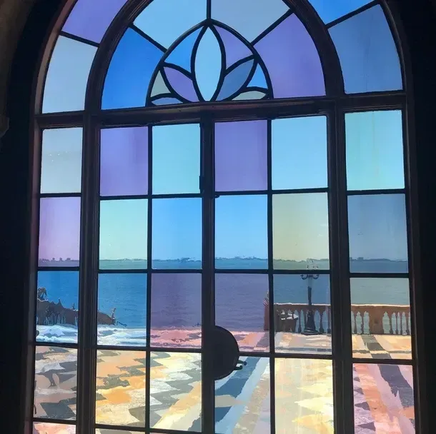 Stained glass window with blue, purple, and green panels overlooking the ocean and a terrace.