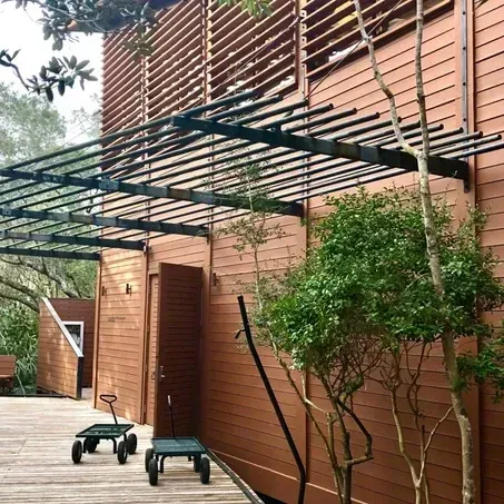 Wooden building with brown siding, dark metal trellis, and green plants.