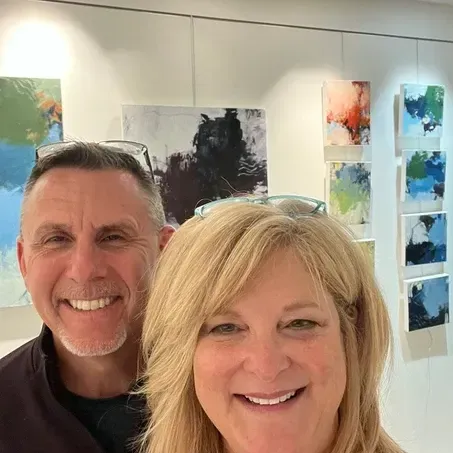 Man and woman smiling in art gallery, surrounded by abstract paintings.