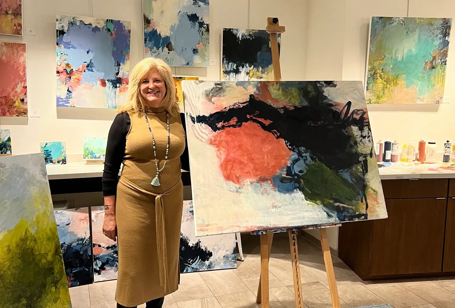 Woman in gallery stands near abstract painting. Artwork on walls in background.