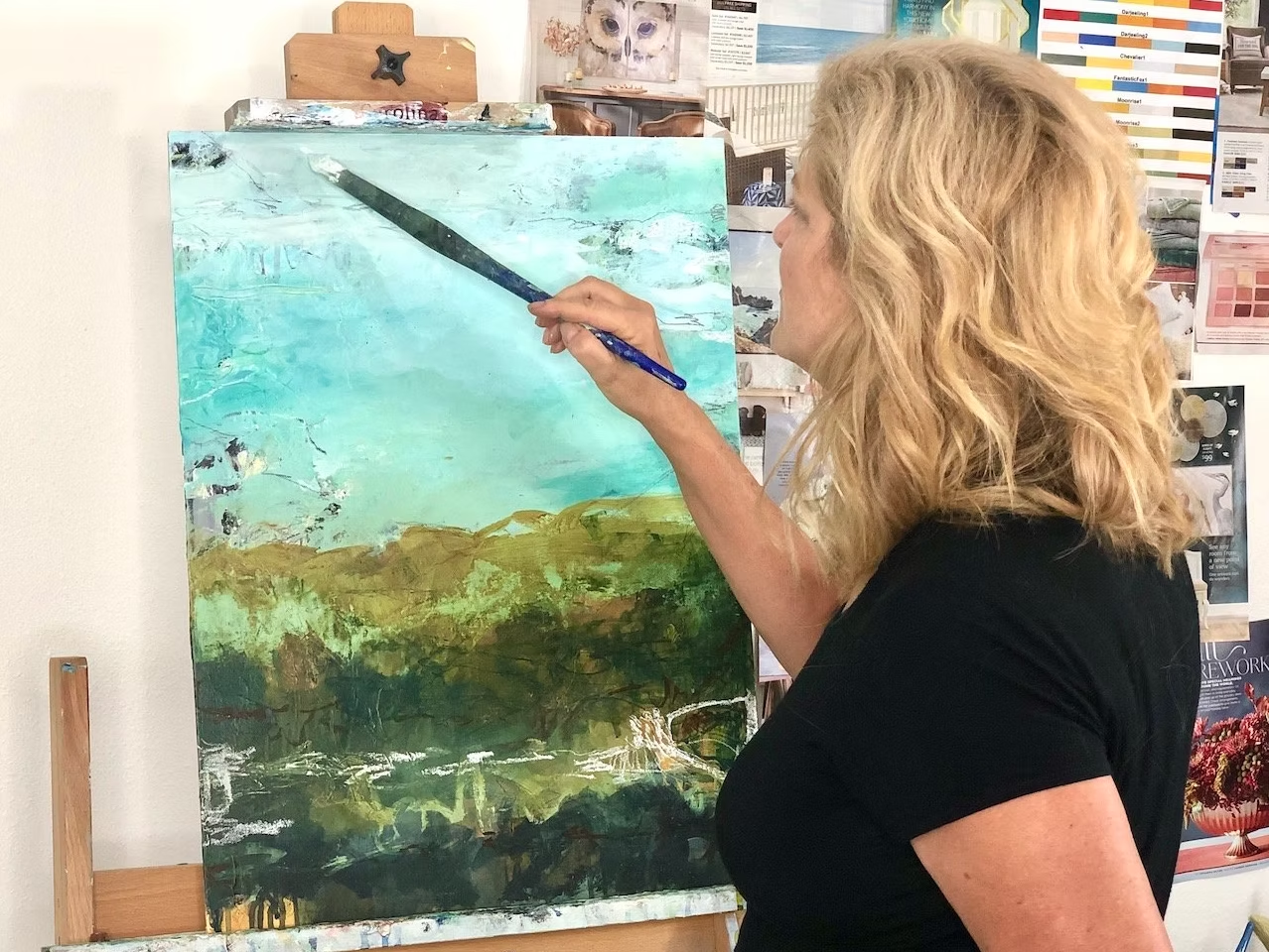 Woman painting on canvas, using a palette knife. Artwork has teal and brown tones.