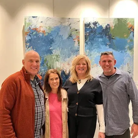 Four people posing in front of abstract blue and green paintings in a gallery setting.