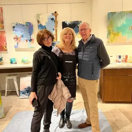 Three people pose in an art studio with colorful abstract paintings.