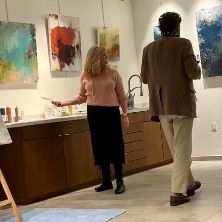 Woman in pink sweater and man in brown jacket viewing art in a gallery.