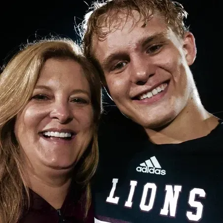 Woman and young man smiling closely. Man in Lions shirt. Dark background.