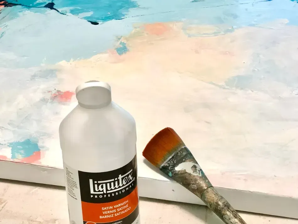 Bottle of Liquitex matte varnish, paintbrush, and abstract painting with blue, pink, and white.