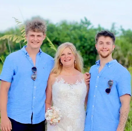 Woman in white dress with two men in blue shirts, posing outdoors.