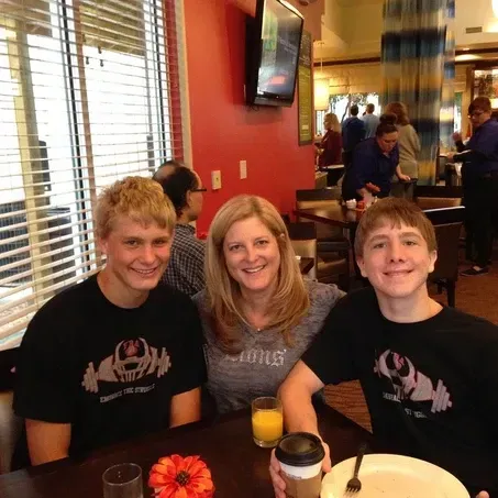 Family sitting at a table in a restaurant. Two young men and a woman smiling, orange juice, and flower on the table.