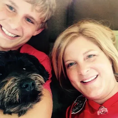 A woman, boy, and black dog smiling, close-up selfie; all are wearing red shirts.