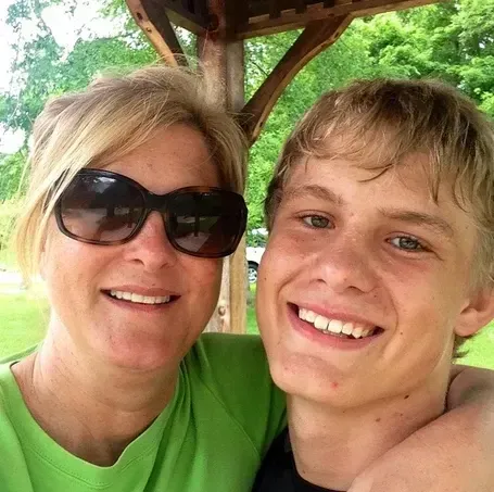 Woman in sunglasses and young person smiling close together outdoors.