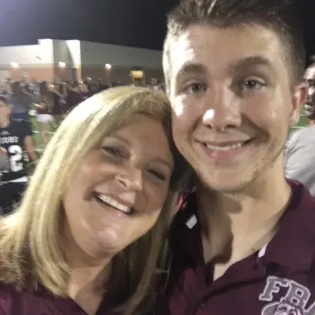 Woman and man smiling close together at a football game, both wearing maroon shirts.
