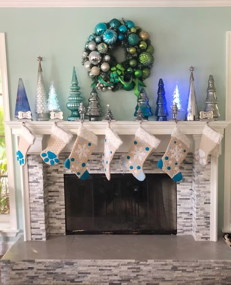 Christmas mantle decorated with blue, silver, and green ornaments, wreath, trees, and stockings.