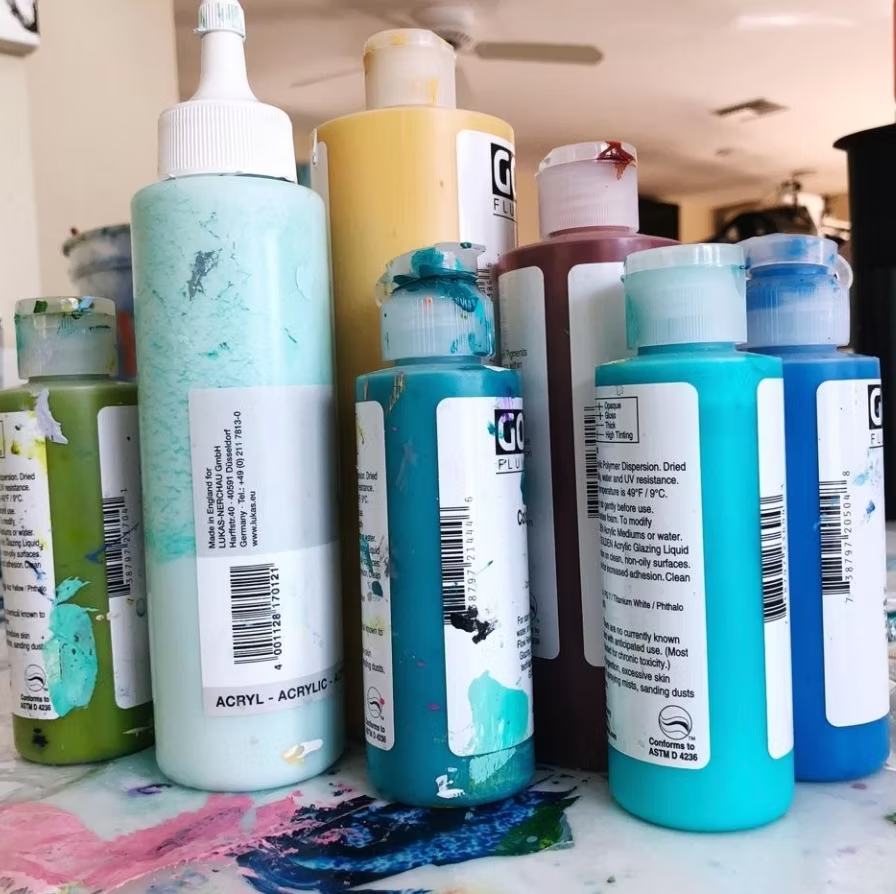 Paint bottles in various colors, including teal, blue, yellow, and brown, on a table.