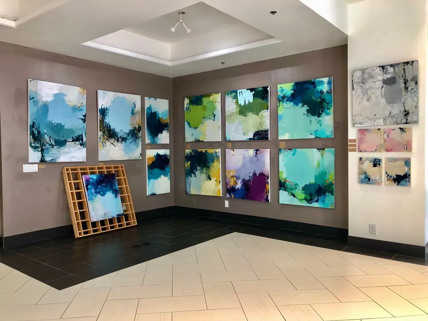 Art gallery with abstract paintings in blues, greens, and purples on a neutral wall.