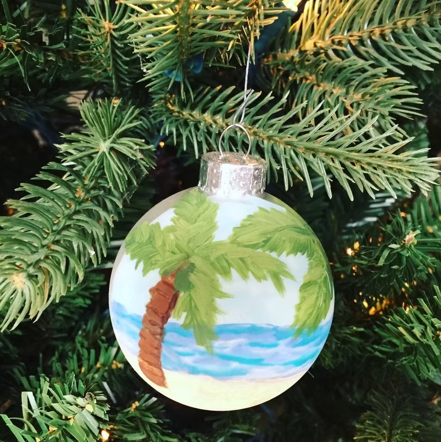 Hand-painted Christmas ornament with palm tree and ocean scene.