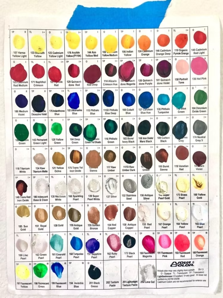 Color swatch chart of acrylic paints with various shades, taped to a clear surface.