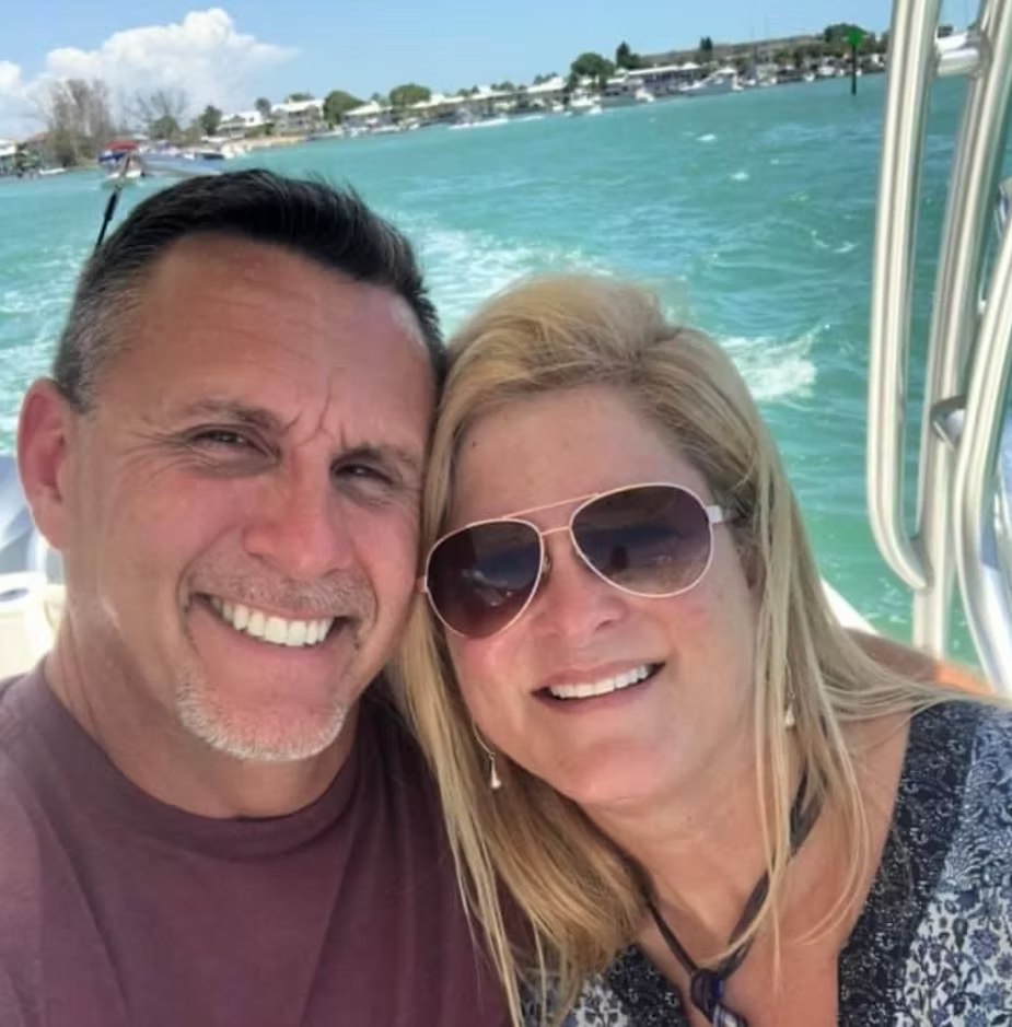 Couple smiling on a boat, turquoise water and buildings in the background.