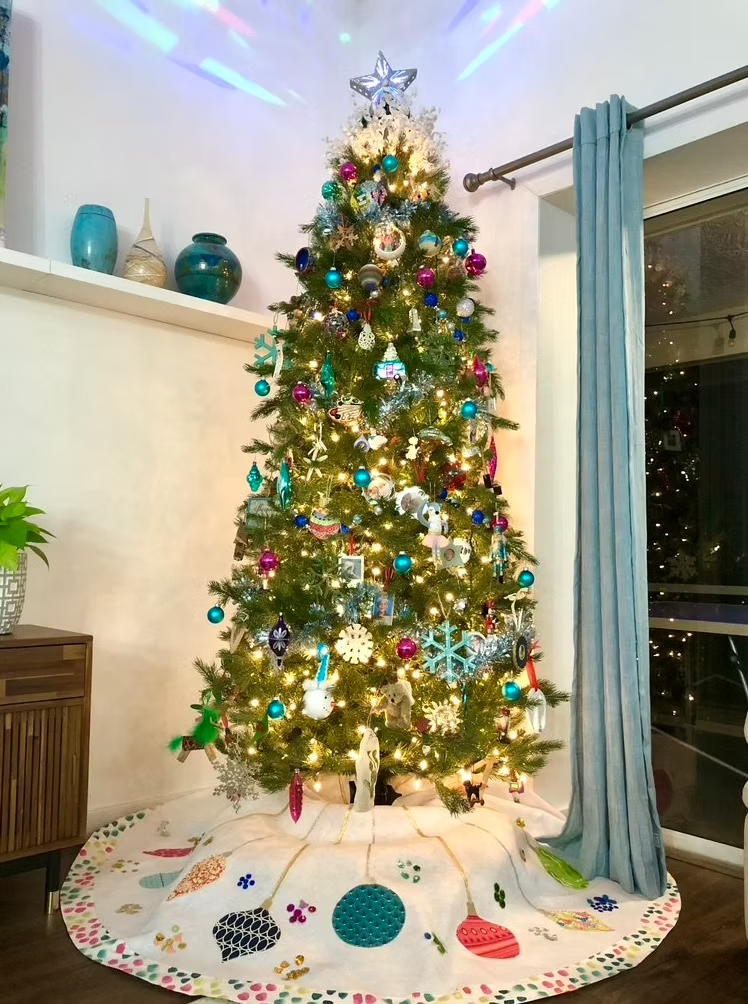 Christmas tree decorated with ornaments, beneath a tree skirt, with a star topper and lights.