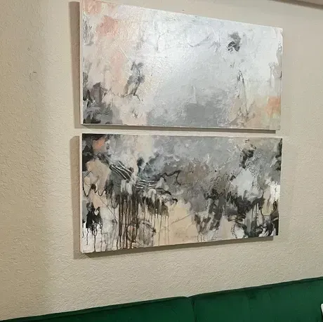 Two abstract paintings on a beige wall, featuring gray, black, beige and pink tones.