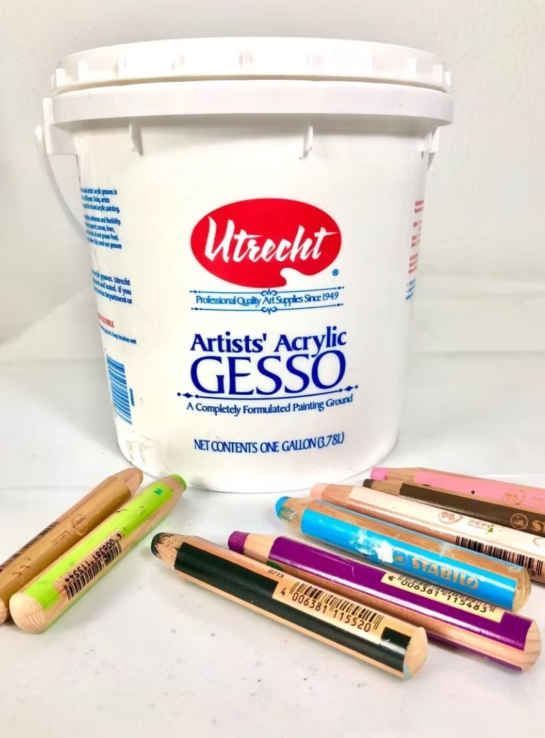 White bucket of Utrecht Artists' Acrylic Gesso with colorful pencils scattered in front.
