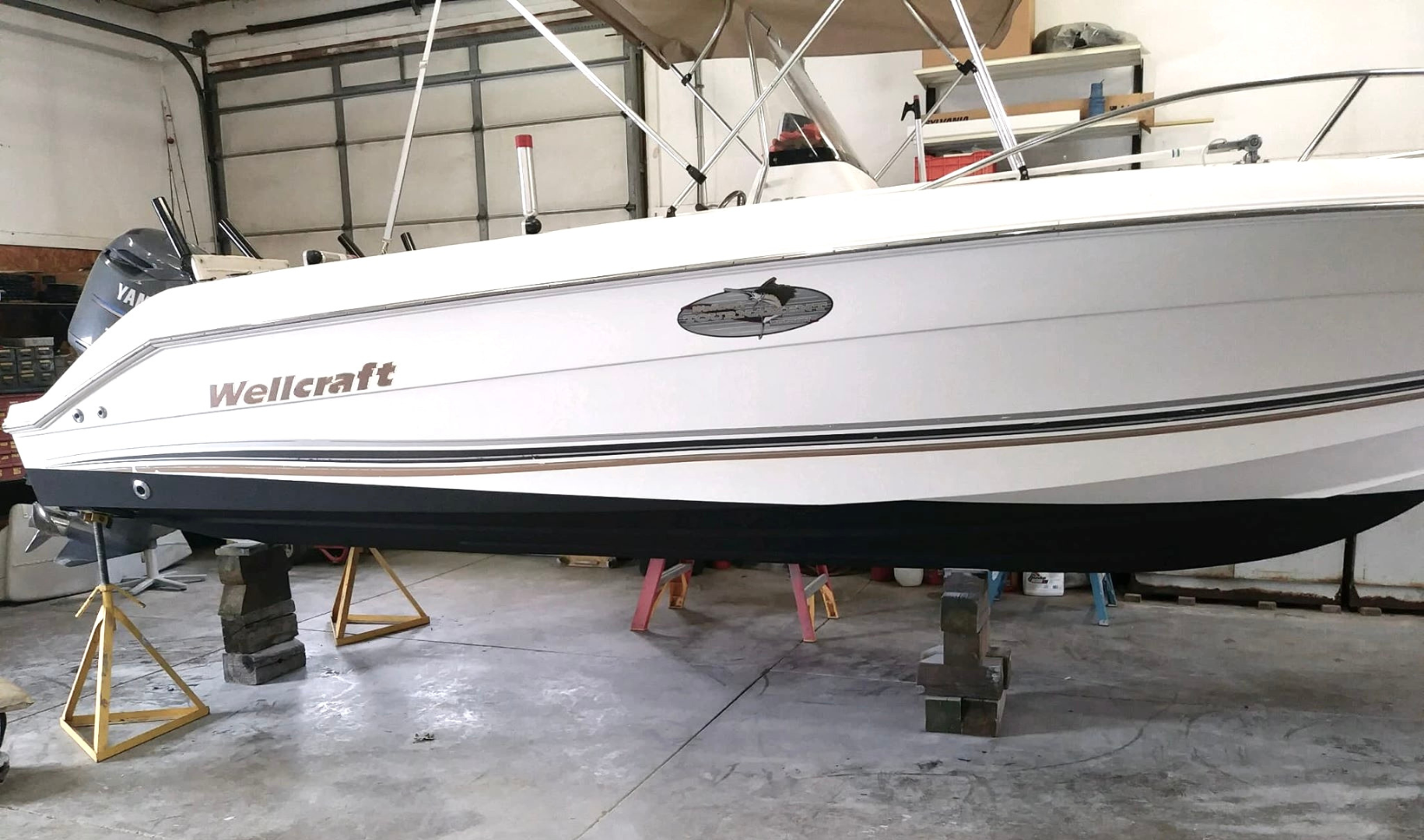 A white boat is sitting on blocks in a garage - boat repair in Huron Ohio.