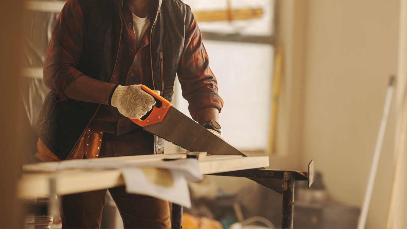 Person using a hand saw to cut wood on a workbench in a workshop