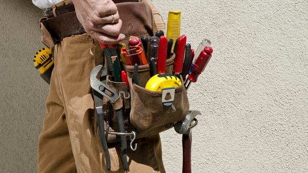 Construction worker’s tool belt with red and yellow hand tools hanging at the waist