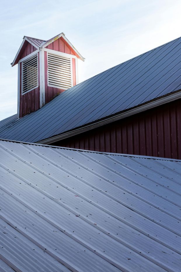 Red barn roof with a small cupola against a bright sky