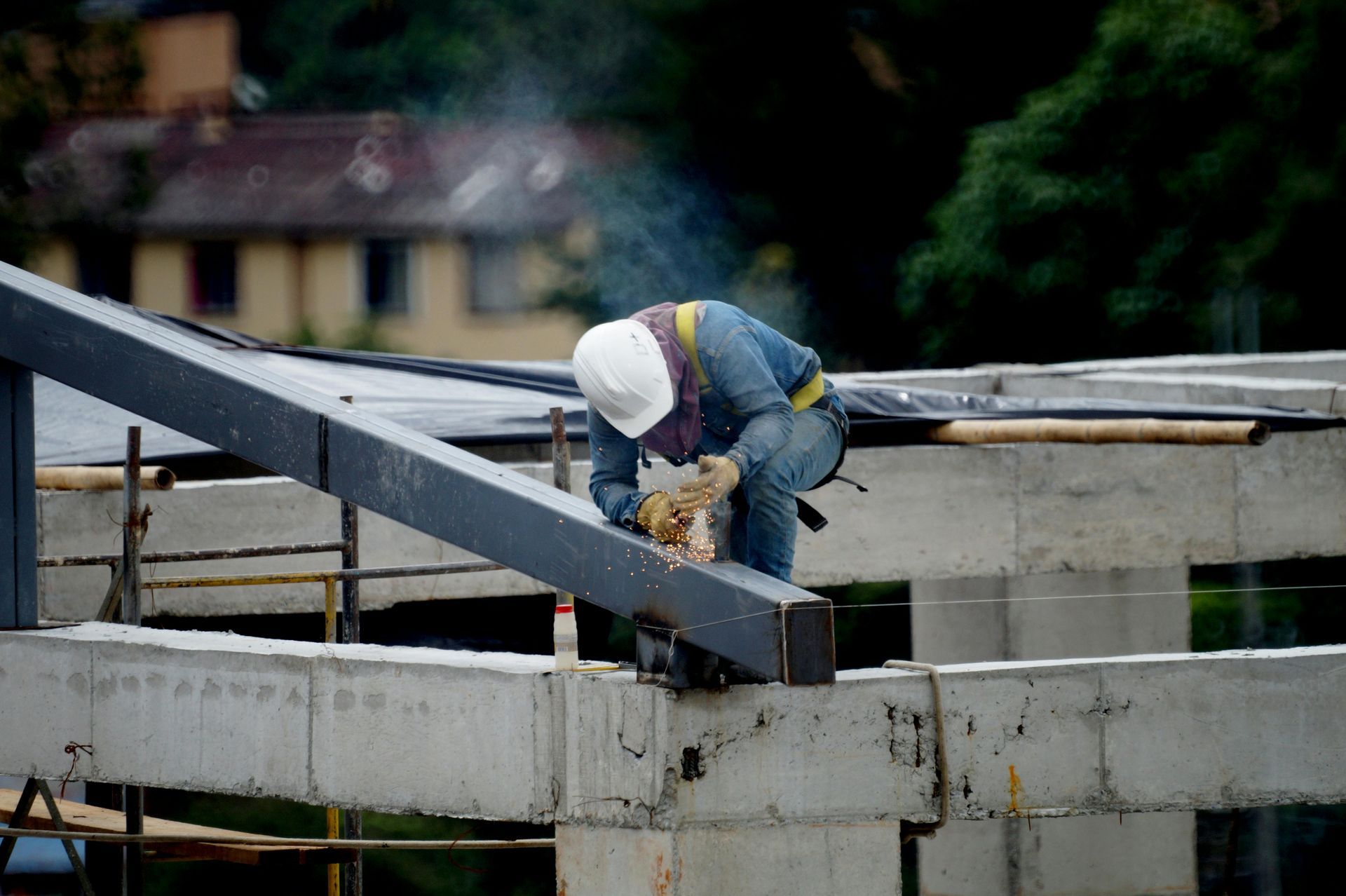 Construction worker in a white hard hat welding a steel beam on a concrete structure.