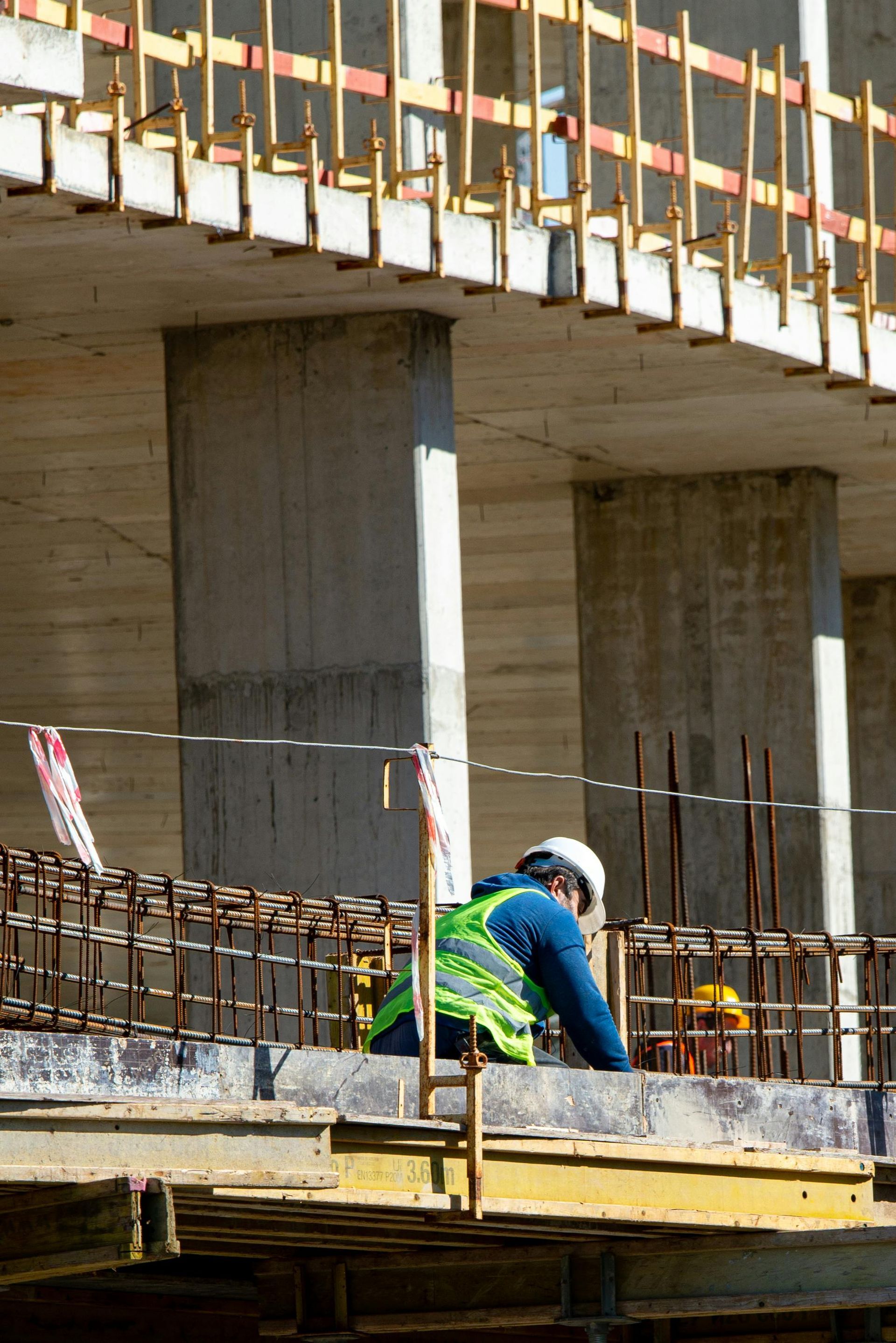 Worker in blue and green safety gear on a concrete construction site under a bridge-like structure