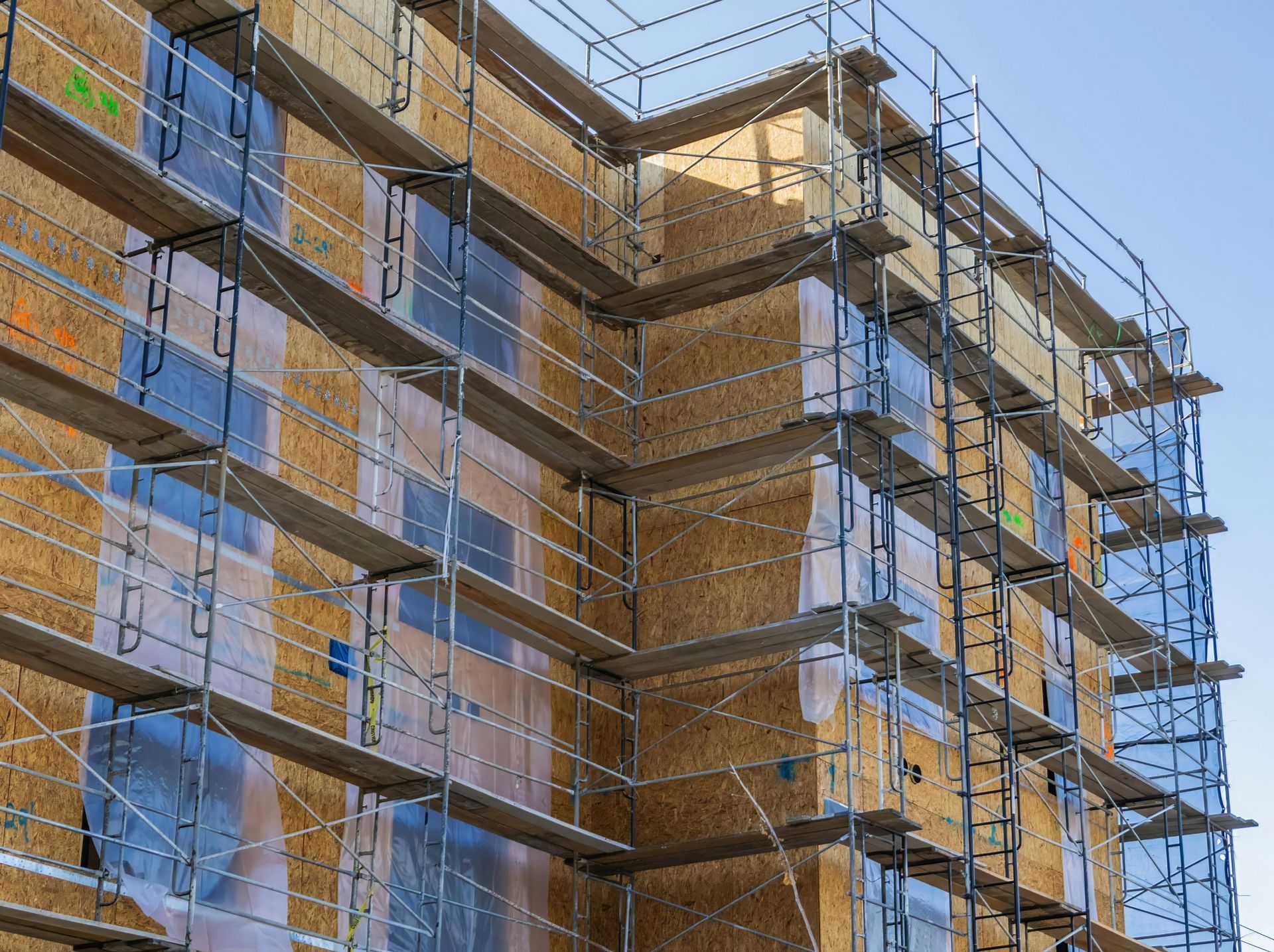 Scaffolding wrapped around a partially built brick apartment building against a blue sky