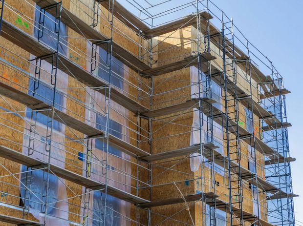 Multi-story building under construction with scaffolding and blue safety netting