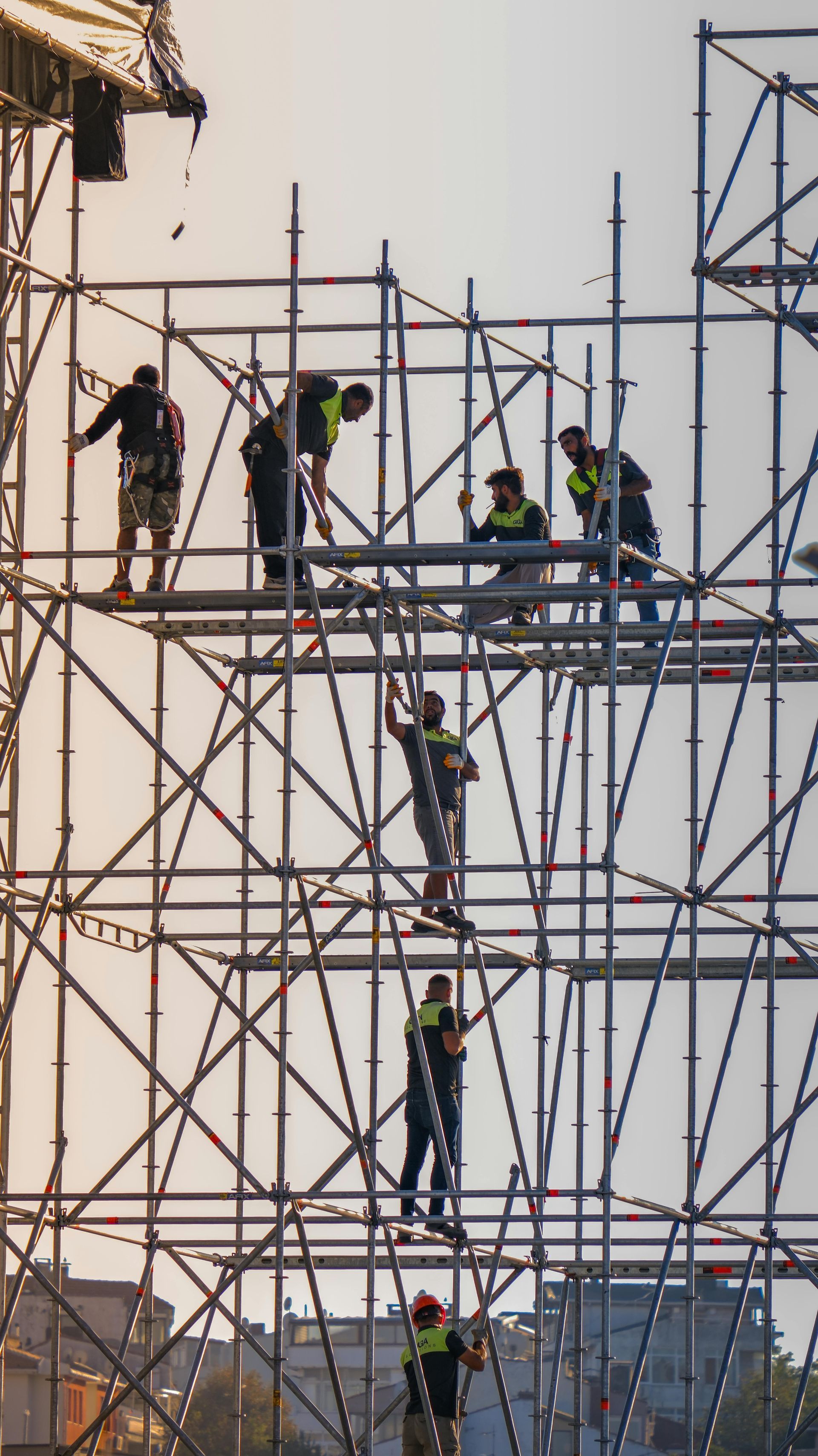 Workers on scaffolding at a construction site, wearing safety vests against a pale sky