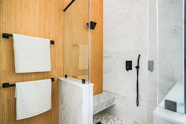 Modern bathroom with wood wall, hanging towels, glass shower, and white marble sink area