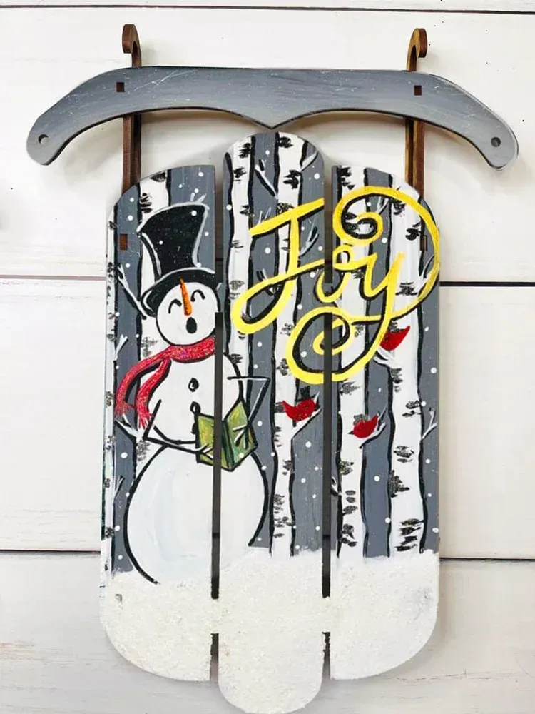 Snowman holding a green book on a white wooden sign with yellow script and striped birch-like background.
