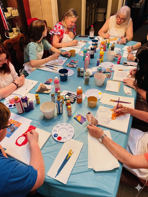 People painting and crafting around a blue-covered table with colorful supplies and brushes
