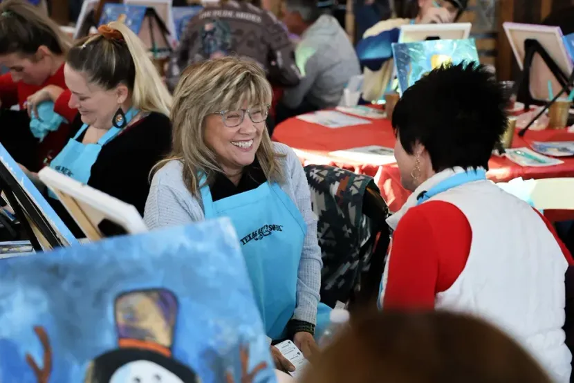 People chatting at a crowded indoor art event, with paintings displayed around them