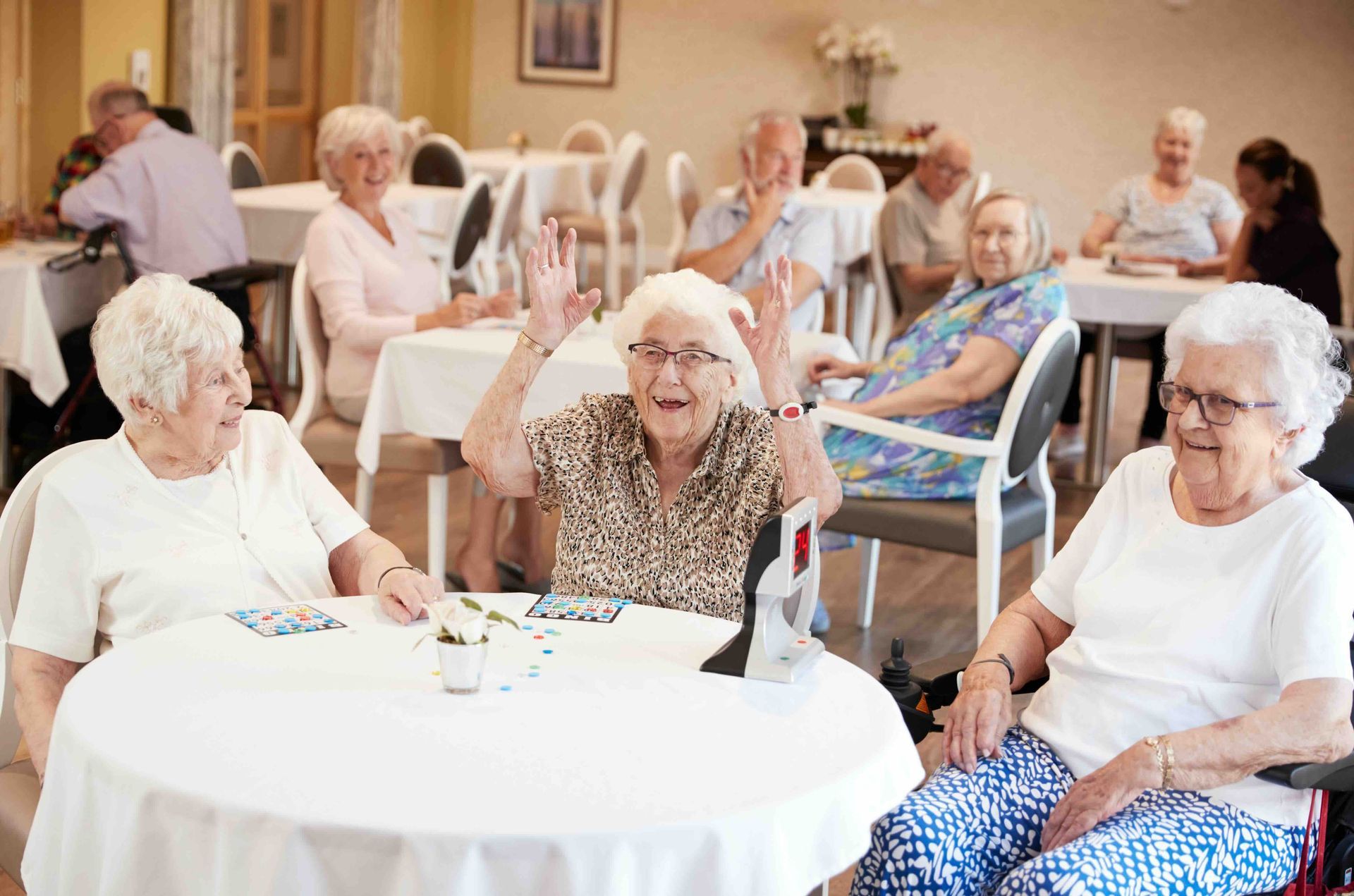 People sitting at round tables in a bright community dining room, chatting and eating
