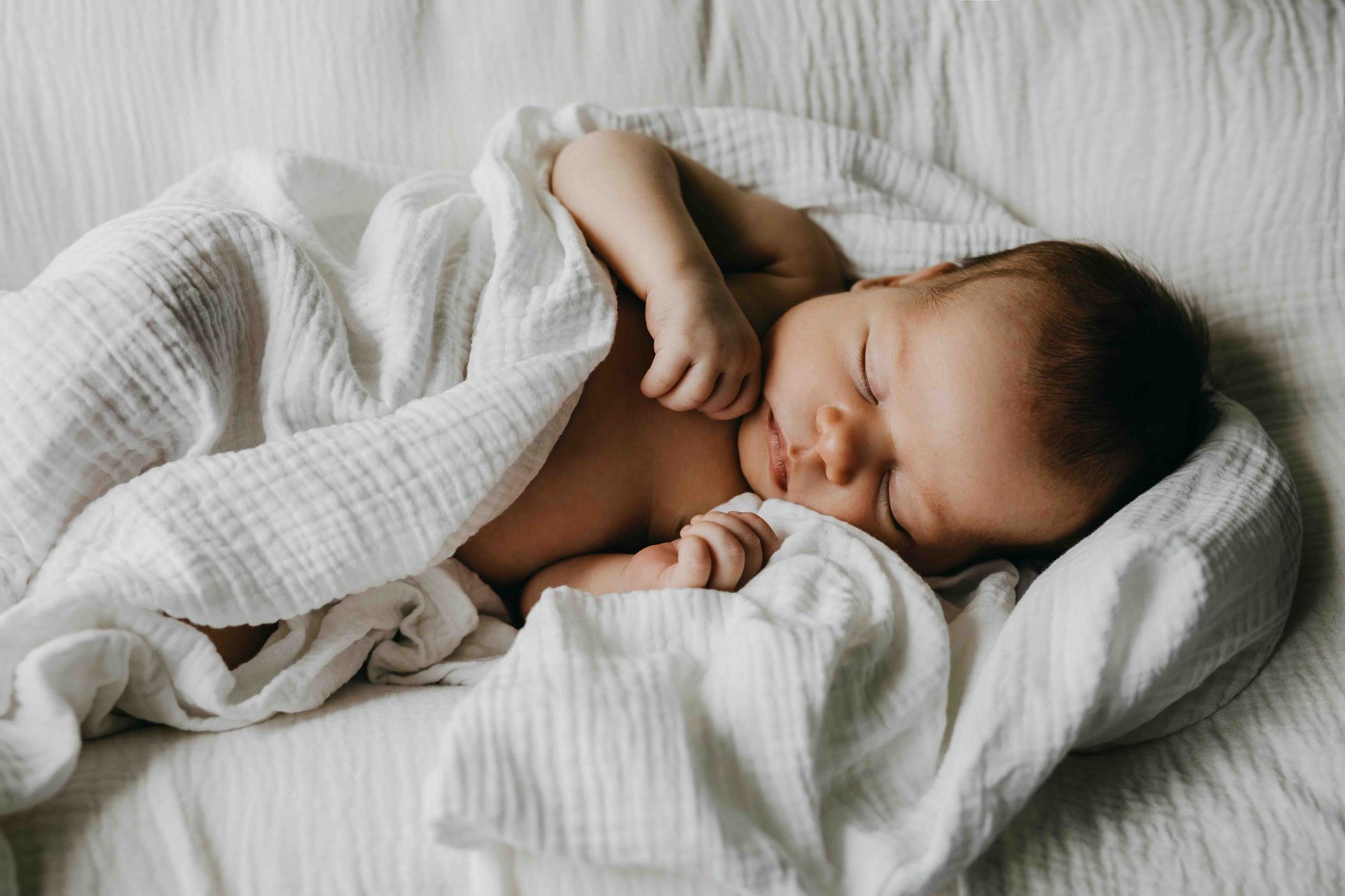 Sleeping baby wrapped in a white blanket on a bed