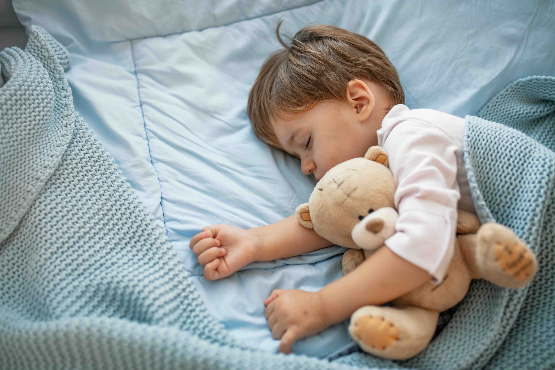 Sleeping child cuddling a teddy bear on a blue blanket