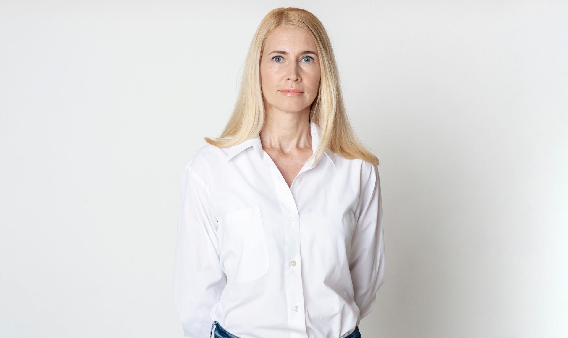 Blonde woman in a white shirt standing against a plain white background