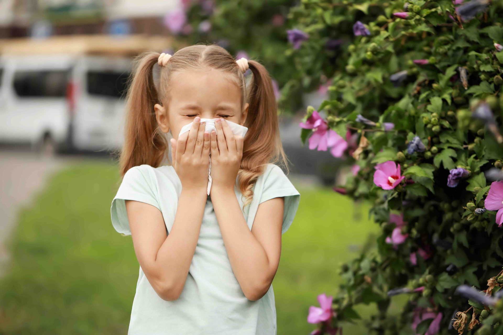 A little girl is blowing her nose in front of flowers.
