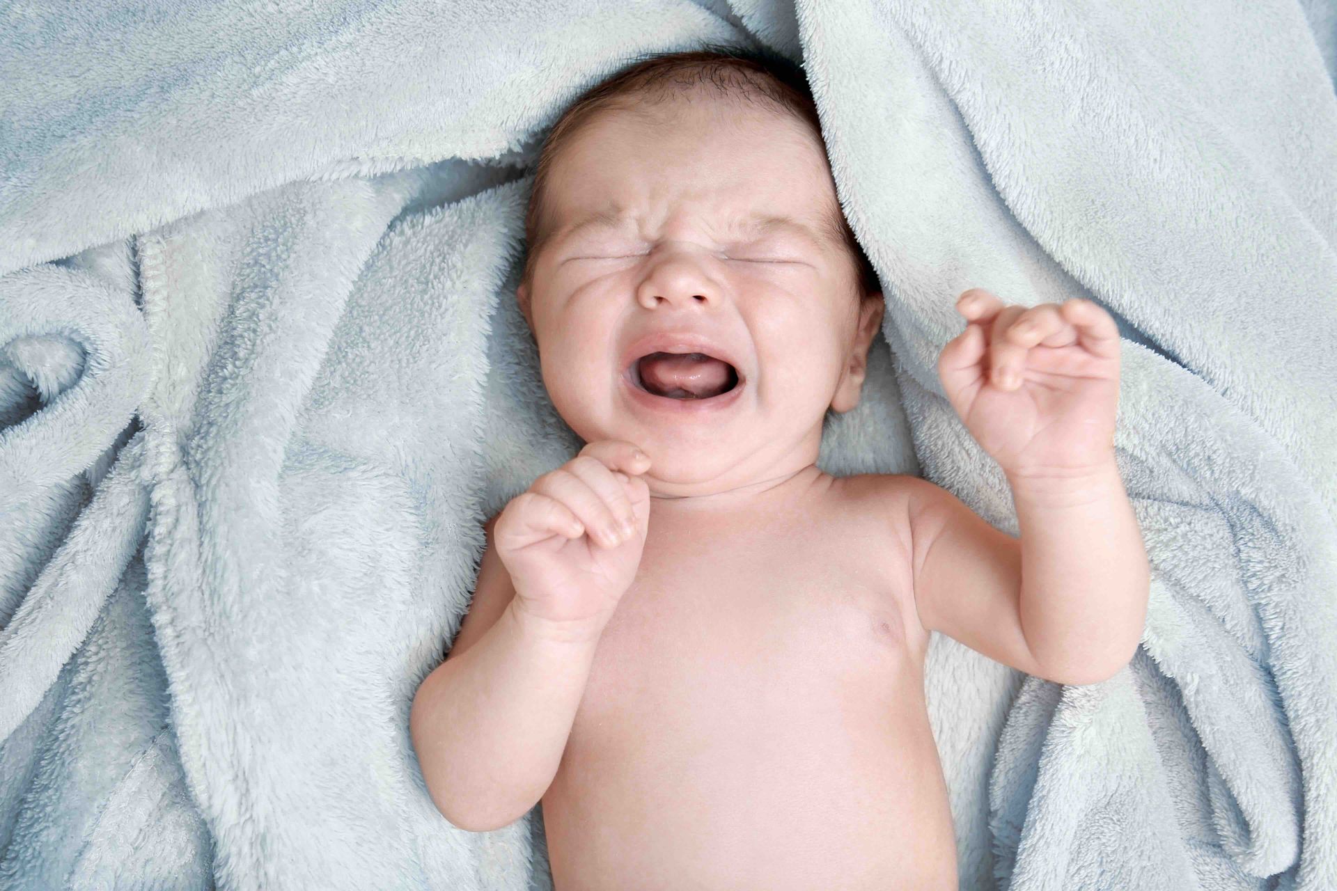A baby is crying while lying on a blanket.