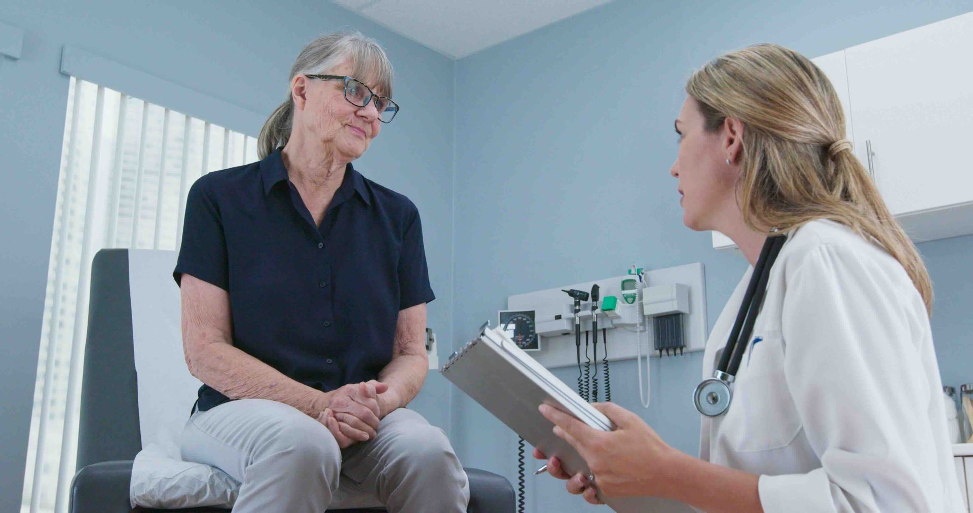 a female doctor is talking to a female patient who is sitting in a chair.