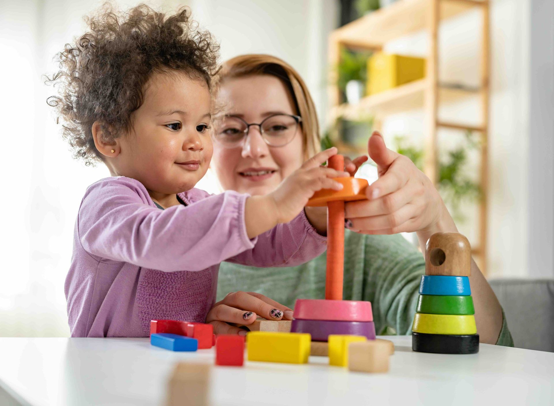 A woman and a little girl are playing with toys at a table.