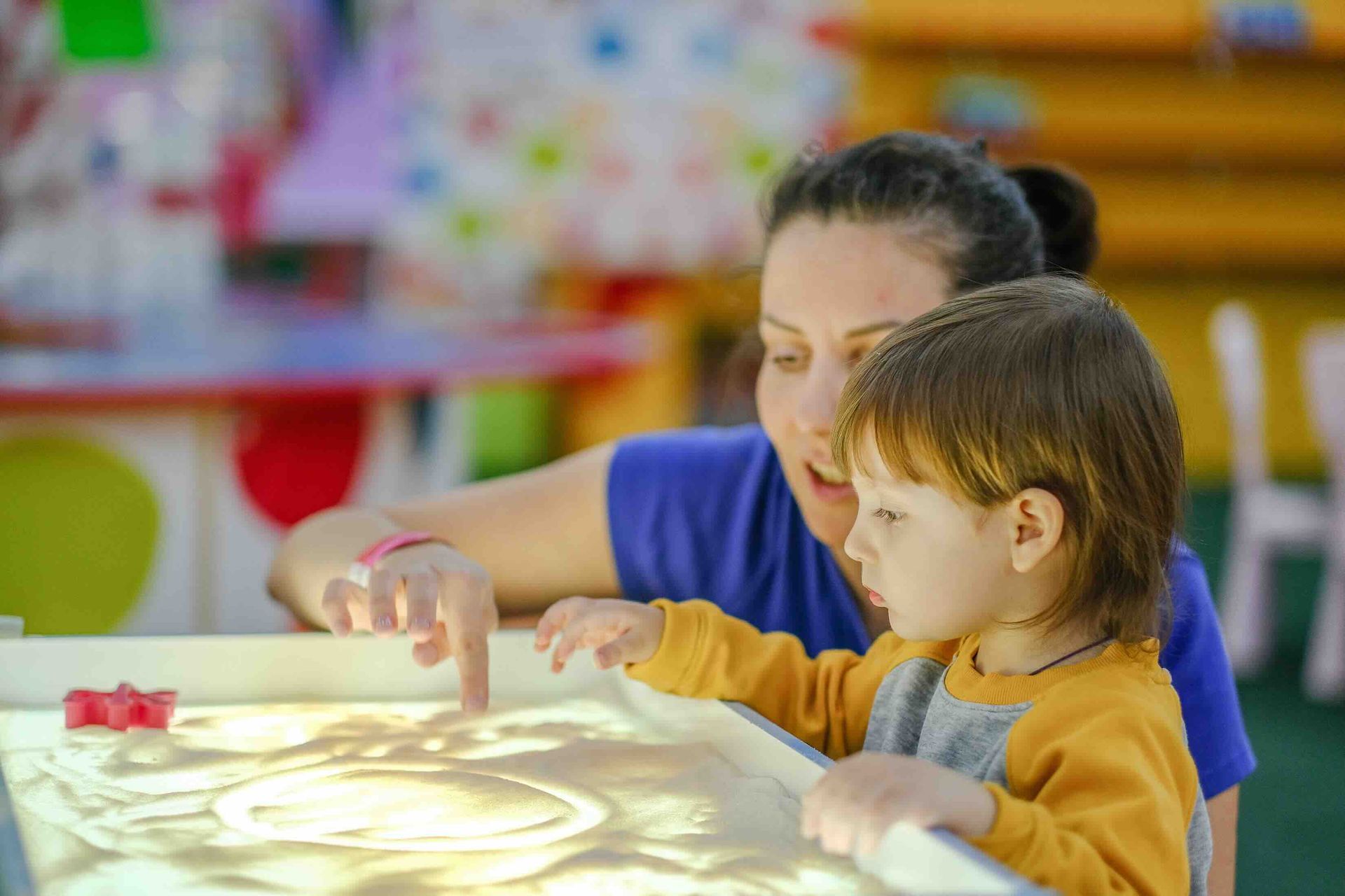 A woman and a child are playing with sand on a table.