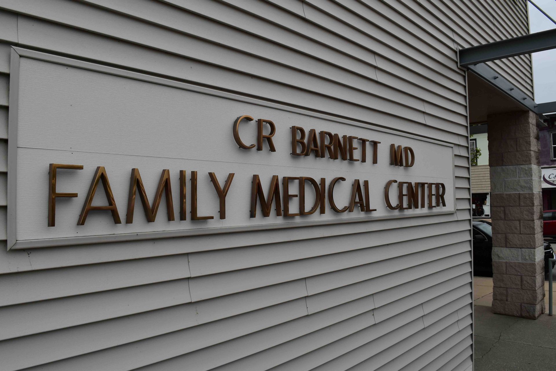 Exterior sign for CR Barnett MD Family Medical Centre on a gray-sided building