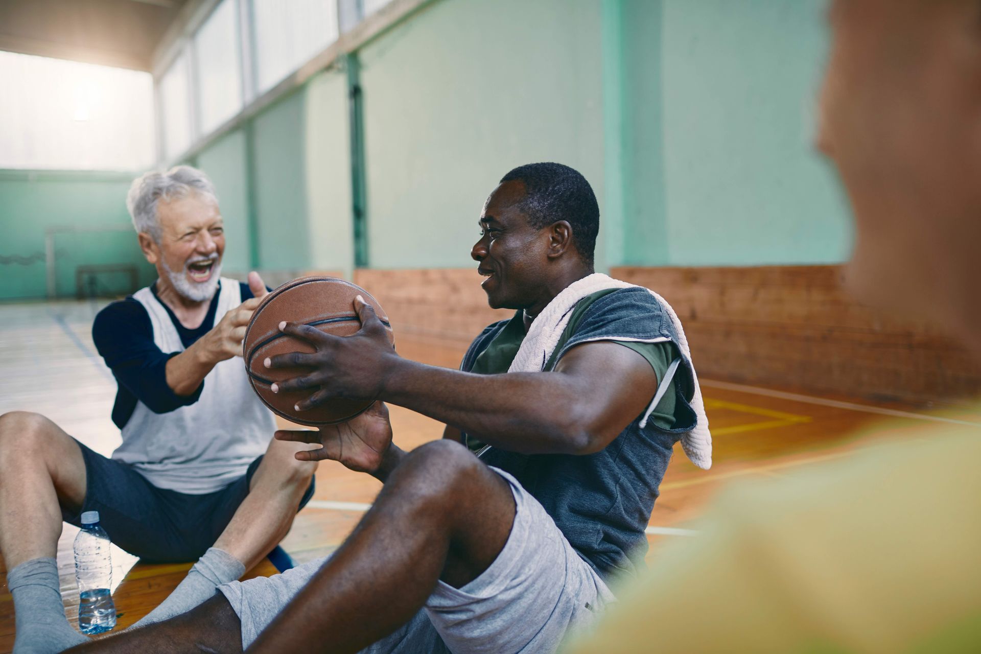 Two people sitting on a gym floor smiling while holding a basketball