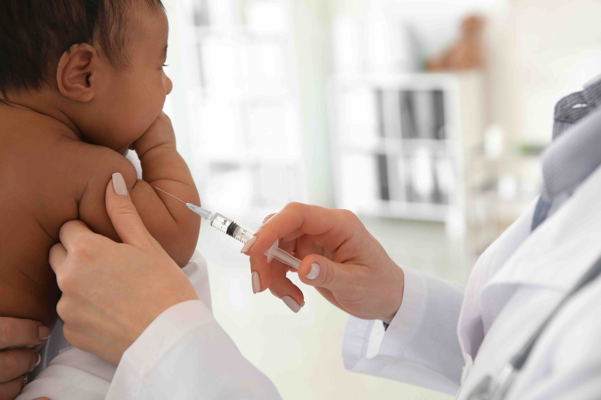 Doctor giving an injection to a baby's arm; clinic setting.