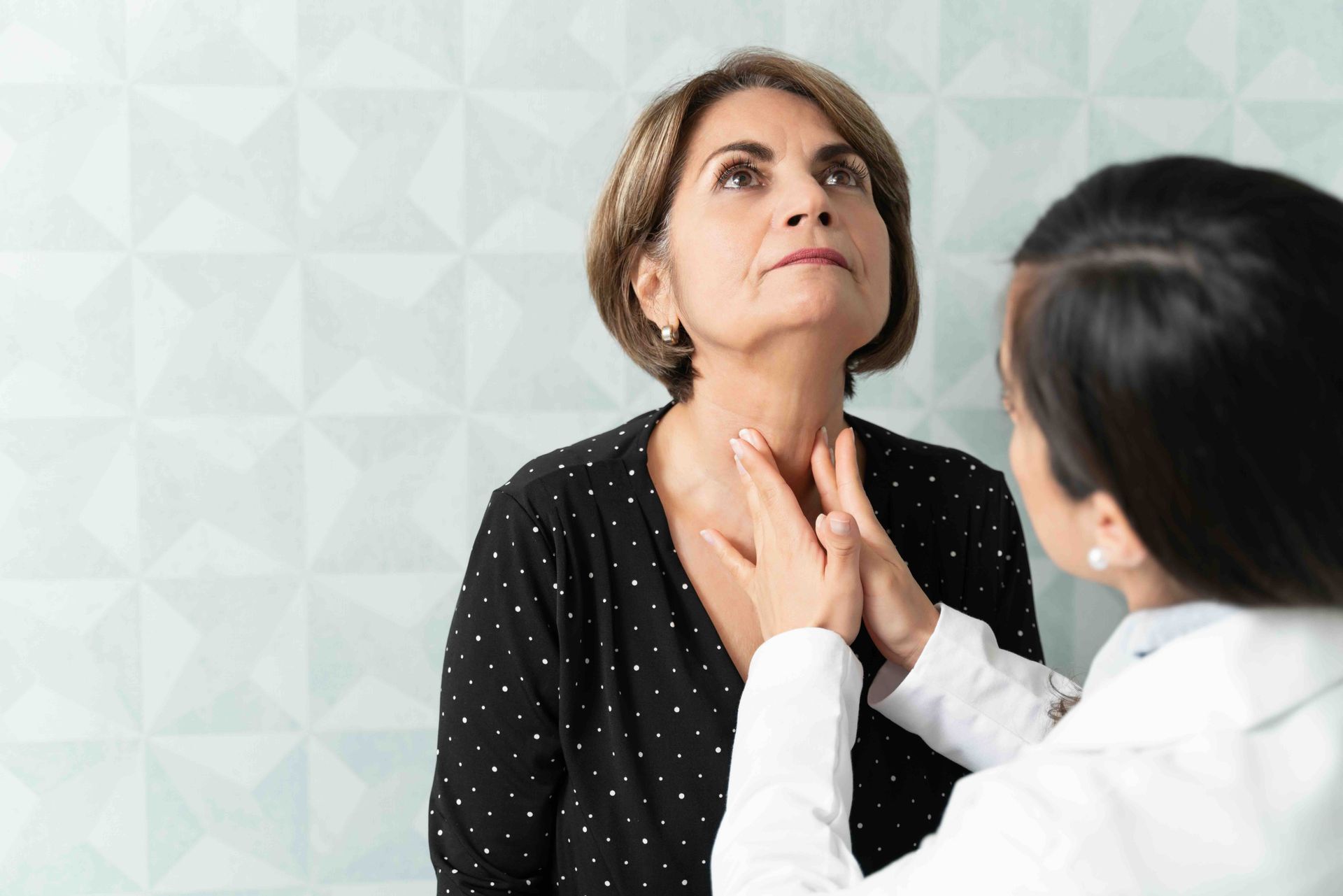 A woman is having her thyroid examined by a doctor.